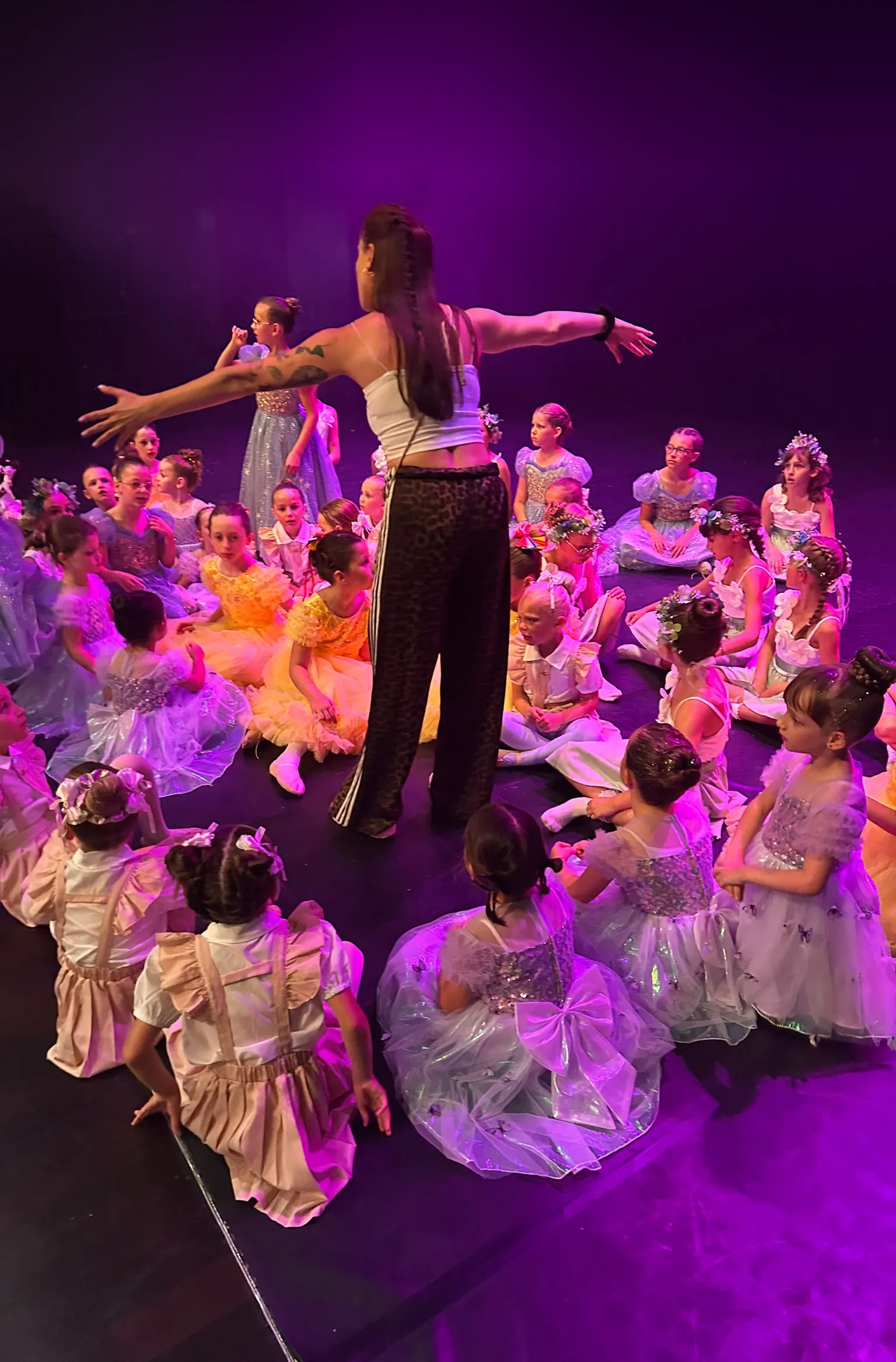 La professeure, bras ouverts, entourée des élèves sur scène pendant le spectacle de fin d’année